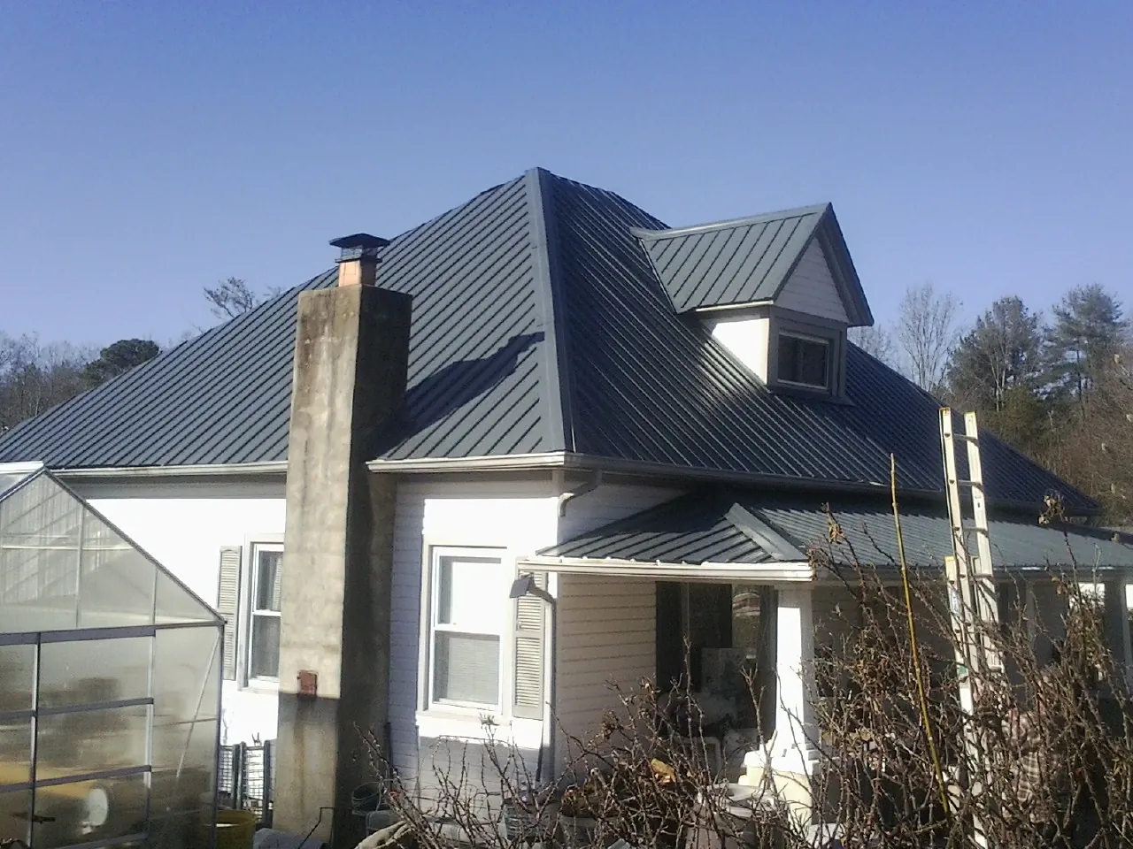 Dark blue standing seam metal roof on a white farmhouse with dormer — Slate & Tile Roof Repair by Roofing Brothers in Byars