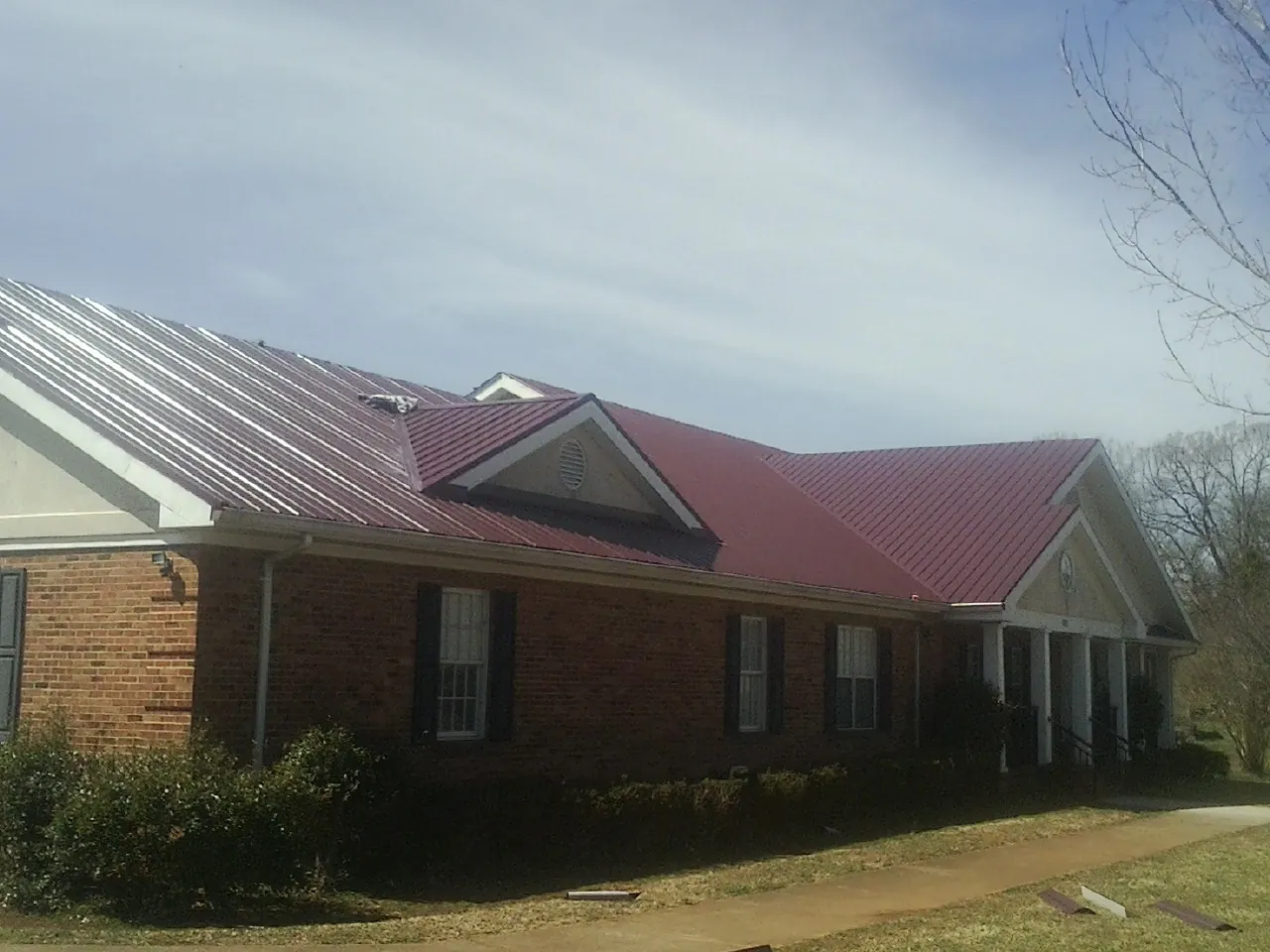 Red metal roof with gabled entries on a long brick building, from a Hail Damage Roof Repair job in Byars