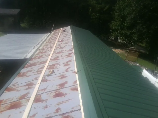 Old rusted panels beside newly installed green metal roofing — Wind Damage Roof Repair by Roofing Brothers in Byars