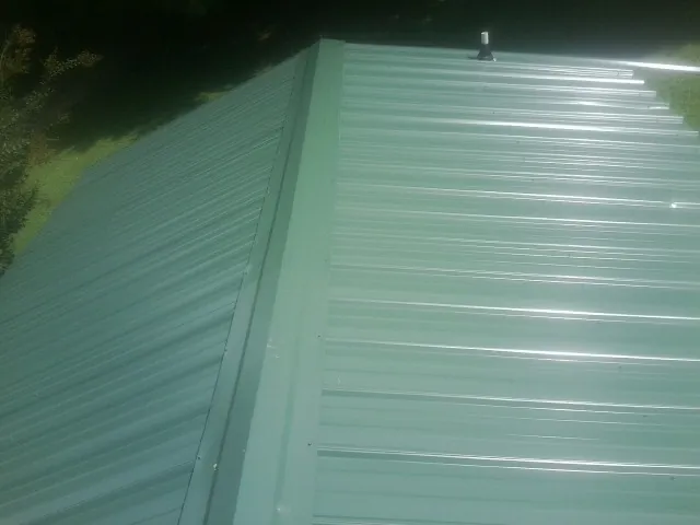 New green metal panels meeting at the ridge of a roof — Flat Roof Repair work by our crew in Byars