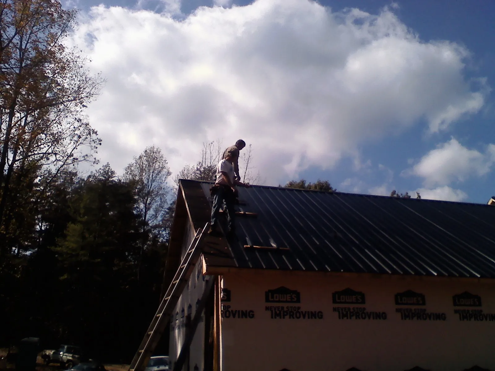 Roofer fastening dark metal panels high against a cloudy sky, from a Roof Inspection job in Byars