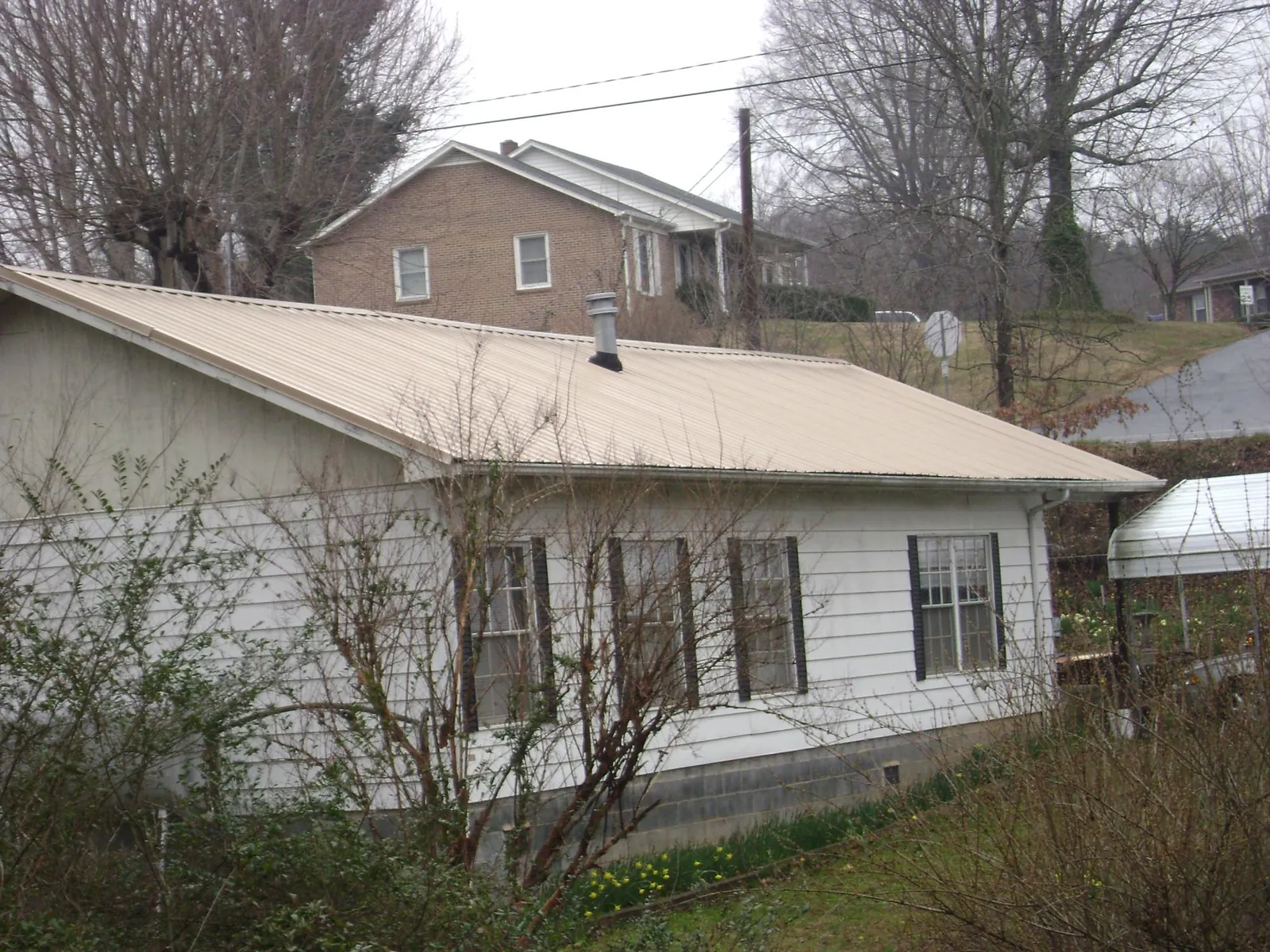 Tan metal roof on a white sided house set into a hillside — Commercial Roofing by Roofing Brothers in Byars