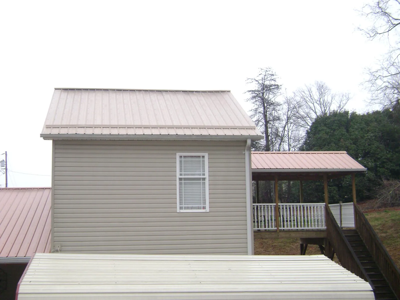 Tan metal roofs on a two story addition and attached porch, from a Roof Replacement job in Byars